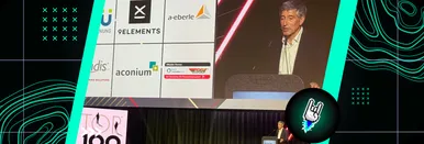 Ranga Yogeshwar auf der Bühne der Top 100-Preisverleihung, im Hintergrund eine Leinwand der Preisträger mit unter anderem dem Logo von 9elements.